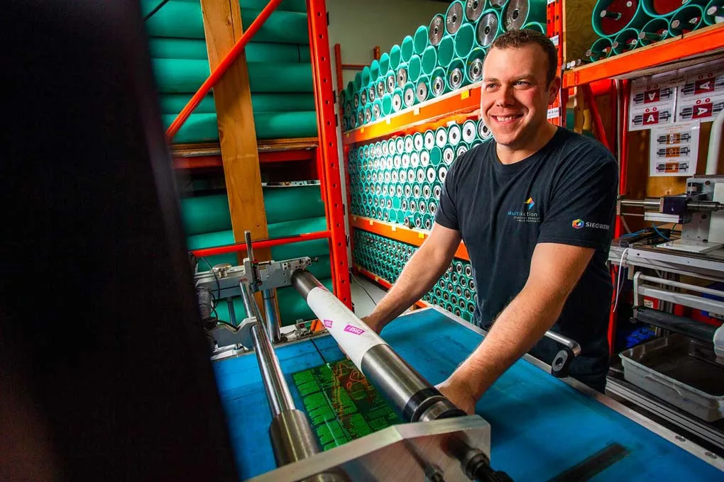 Custom label printing expert smiling while operating flexographic printing press for high-quality labels.
